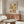 May include: Paul Klee exhibition poster with abstract botanical motifs in warm yellow, orange and brown geometric blocks, displayed above a mid-century walnut credenza in a modern living room with cream walls, white curved chair, glass oval coffee table, and minimalist floor lamp