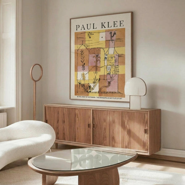 May include: Paul Klee exhibition poster with abstract botanical motifs in warm yellow, orange and brown geometric blocks, displayed above a mid-century walnut credenza in a modern living room with cream walls, white curved chair, glass oval coffee table, and minimalist floor lamp