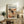 May include: Framed Jackson Pollock exhibition poster featuring abstract drip painting with black paint splatters, orange and beige tones, and chaotic linear marks on cream background. Light wood frame sits on rustic wooden sideboard next to fern plant, books, and ceramic vases in warm neutral living room setting.