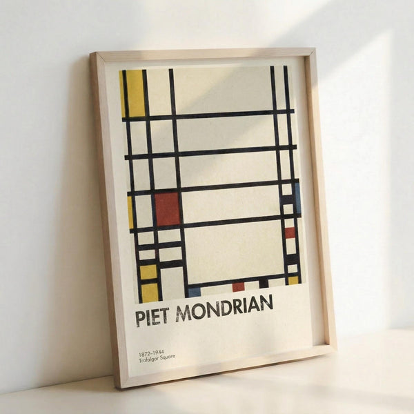 May include: Framed art print featuring Piet Mondrian's geometric abstract composition with black grid lines and rectangular blocks in yellow, red, and blue on cream background. Artist name and dates "1872-1944" with "Trafalgar Square" printed below artwork. Light wood frame leaning against white wall, showing natural lighting and shadows on the glass surface.