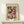 May include: Framed poster featuring Paul Klee's abstract geometric artwork with colorful squares and rectangles in reds, greens, blues, and earth tones, displayed on a light wood shelf against a cream wall. Small white gift box with twine and evergreen sprig sits in front of the natural wood frame.