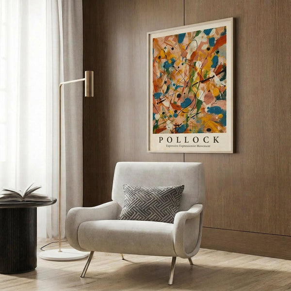 May include: Abstract expressionist art poster with vibrant orange, blue, and yellow paint splatters and black lines in white frame, hanging on wood-paneled wall above beige upholstered armchair with geometric patterned pillow, brass floor lamp with white circular base nearby
