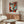 May include: Framed Picasso-style cubist face poster with geometric shapes in red, orange, teal, and cream colors hanging above wooden credenza in modern living room. White sculptural chair, glass coffee table, and contemporary lamp visible. Abstract portrait features fragmented facial elements in bold angular design.