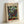 May include: Framed poster of Paul Klee's abstract artwork featuring a mosaic-like grid of colorful painted squares in greens, blues, purples, reds, and earth tones. The print has a cream-colored border with "PAUL KLEE" at the top and "MAY PICTURE - THE MET MUSEUM" at the bottom. Displayed in a light wooden frame leaning against a white wall on a light surface.