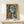 May include: Framed Picasso-style cubist portrait print featuring abstract woman with geometric blue and orange forms, displayed on light wood console table beside small wrapped gift with twine, against cream wall in minimalist home setting