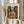 May include: Person in cream clothing holding framed Picasso-style cubist artwork showing angular musician figure in brown, orange and beige tones playing guitar, with dried pampas grass visible to left, against neutral curtained background