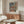 May include: Framed Picasso-style art print featuring a woman in colorful traditional dress with red and blue striped skirt, displayed above a mid-century modern walnut credenza in a minimalist living room with white upholstered chair, glass coffee table, and warm lighting