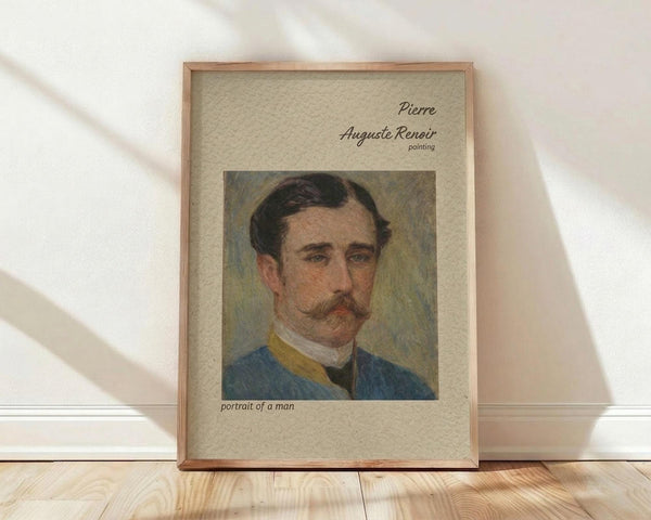 May include: Framed poster print featuring a portrait painting of a man with dark hair and mustache wearing a blue jacket with yellow collar detail. The artwork is displayed in a light wooden frame with beige matting, leaning against a white wall on light wood flooring with natural sunlight casting diagonal shadows across the scene.