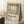 May include: A framed Mondrian-style abstract art poster with geometric black grid lines and blocks of yellow, red, and blue on cream background, leaning against white walls in a cozy corner with textured rug, wooden side table with white coffee cup, and beige knit blanket visible in natural lighting.