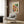 May include: Framed Paul Klee abstract watercolor print with colorful geometric squares in blues, greens, oranges, and purples hanging on wood-paneled wall above cream upholstered armchair with geometric patterned pillow, next to brass floor lamp and dark round side table with open book