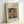 May include: Framed vintage-style poster print featuring a painted portrait of a mustachioed man in blue military uniform with yellow collar details. The artwork shows impressionistic brushwork with warm skin tones against a muted background. Text reads "Pierre Auguste Renoir painting" and "portrait of a man" on cream-colored paper. Light wood frame displayed leaning against white wall on white surface with soft natural lighting.