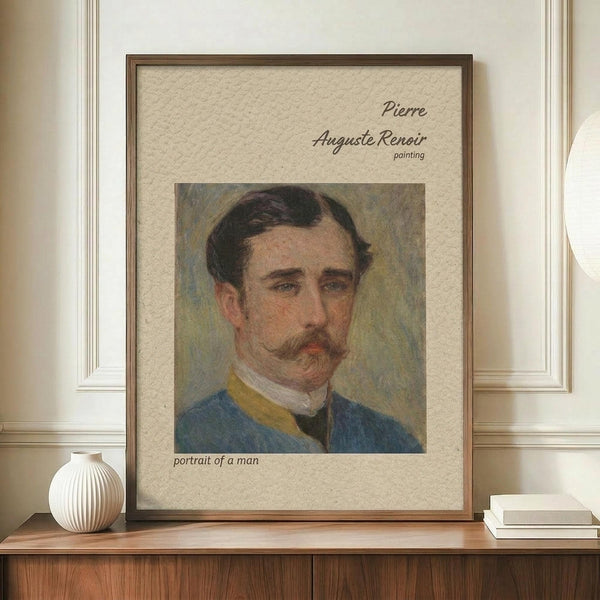 May include: Framed art print featuring a vintage portrait of a man with dark hair and mustache wearing a blue jacket with yellow collar details. The artwork has an impressionistic painting style with soft brushstrokes and muted colors. The print is displayed in a thin brown wooden frame on a wooden sideboard alongside a white ribbed ceramic vase and stacked books, against cream colored walls with white wainscoting.