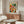May include: Colorful abstract watercolor artwork poster with geometric squares in vibrant reds, blues, greens, yellows and purples, displayed in thin frame above mid-century modern walnut credenza. Room features white curved chair, glass oval coffee table, brass floor lamp with circular shade, and modern table lamp. Minimalist interior with white walls and natural lighting creates clean contemporary aesthetic.