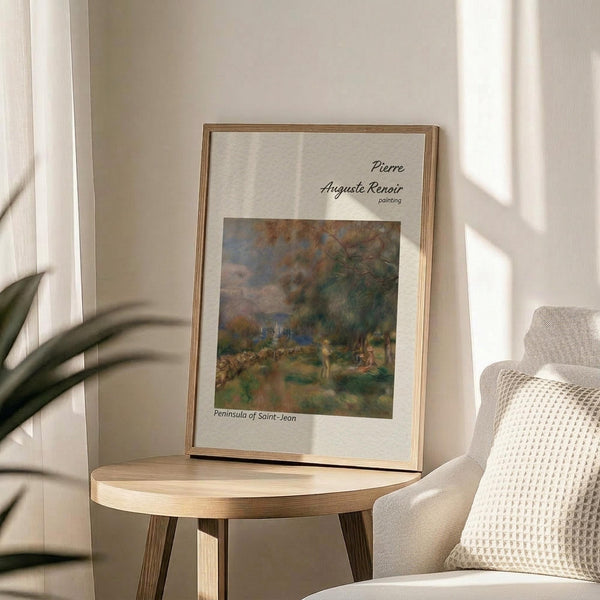 May include: Framed reproduction of Renoir's impressionist landscape painting showing the Peninsula of Saint-Jean with soft greens, browns, and blues depicting trees, figures, and water. The print is displayed in a thin wooden frame on a round wooden side table next to a beige upholstered chair with white textured pillow, near a plant and white curtains in natural sunlight.