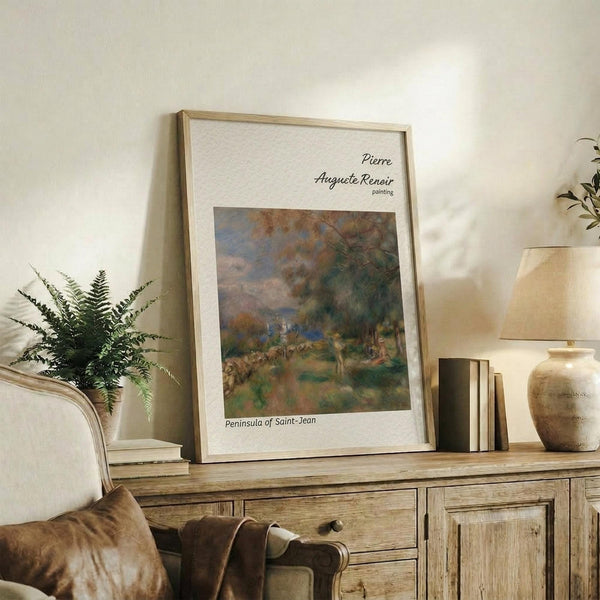 May include: Framed Renoir painting print displayed on rustic wooden sideboard in warm neutral living room setting. Features impressionist landscape artwork with soft greens, browns and blues depicting countryside scene. Natural wood frame complements fern plant, cream lamp, ceramic vase and books on console table beside beige upholstered chair.