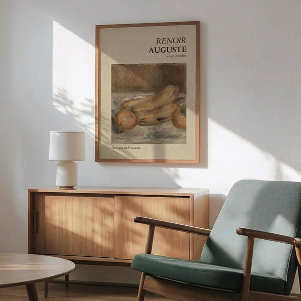 May include: Framed Renoir poster featuring oranges and bananas still life painting in warm tones, displayed above a mid-century wooden sideboard with white table lamp, next to sage green upholstered armchair with wood frame in sunlit modern living room with white walls.