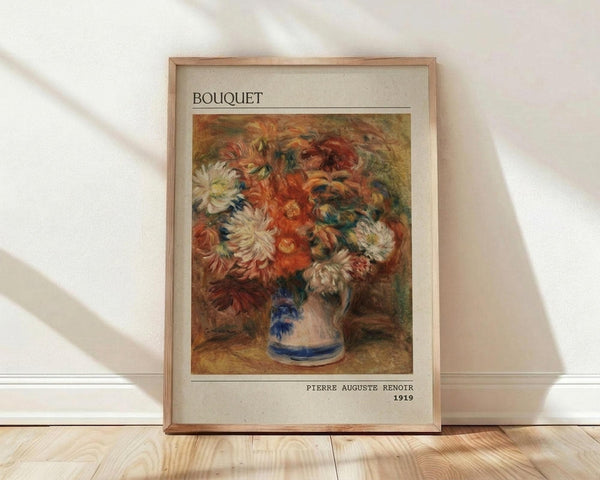 May include: Framed art print of Pierre Auguste Renoir's 1919 floral painting showing vibrant orange and red flowers with white chrysanthemums in a blue and white ceramic vase. The impressionist-style bouquet features warm autumn colors against an earthy brown background. Light wood frame with cream matting displays the artwork against a white wall on light wooden flooring with natural sunlight casting diagonal shadows.