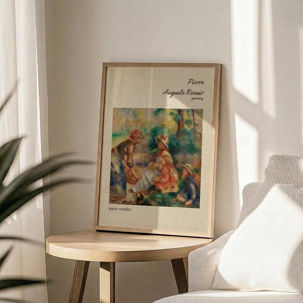 May include: Framed art print of Renoir's colorful Impressionist painting showing figures in a garden scene with warm reds, greens, and earth tones, displayed on a round wooden side table next to a beige upholstered chair with natural sunlight casting shadows across white walls and green plant leaves visible in corner of bright, minimalist room setting.