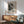 May include: Abstract black and white art poster with splattered paint design in wooden frame, displayed above mid-century modern wooden sideboard with ceramic lamp. Sage green upholstered chair with wooden arms sits nearby on hardwood floor with natural sunlight streaming across white walls.