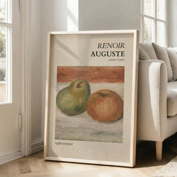 May include: Framed art print leaning against beige sofa in bright living room with large windows. Print shows Renoir still life painting of green pear and red apple on white surface. Light wood frame, cream matting, natural sunlight streaming across wooden floors.