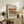May include: Framed art print featuring Auguste Renoir's still life painting of green pears and a red apple on neutral background. Print displayed on rustic wooden sideboard with cream upholstered chair, potted fern, ceramic vase, and stacked books in warm-toned living room setting.