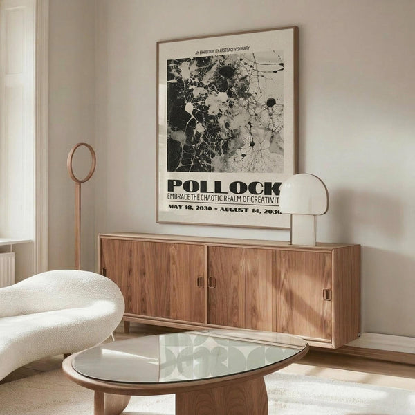 May include: Abstract black and white art poster with Pollock text and exhibition details, displayed above wooden mid-century sideboard in neutral living room. White upholstered chair and glass coffee table visible. Poster features splattered paint texture in monochrome tones with bold typography below the artwork.