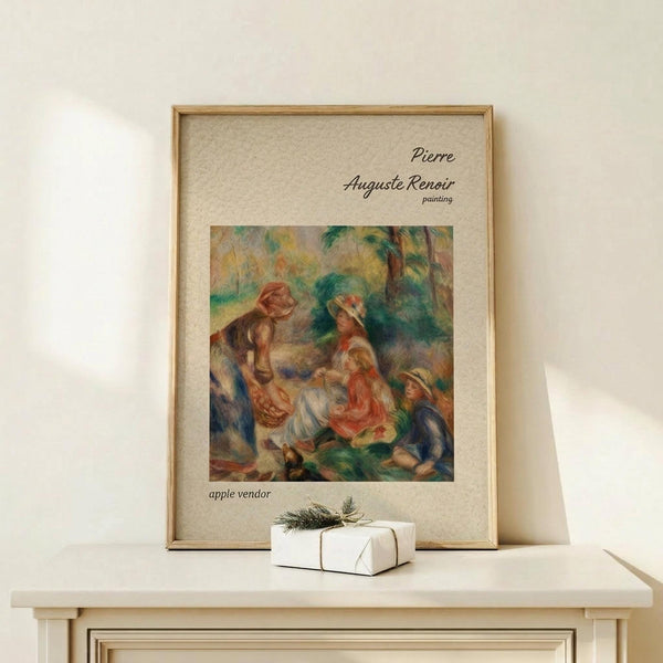 May include: Framed art print of Renoir's impressionist painting showing figures in a outdoor scene with warm colors of orange, green, and blue. The wooden frame sits on a light wood shelf next to a small wrapped white gift box with twine and greenery. Cream colored wall background with soft natural lighting.
