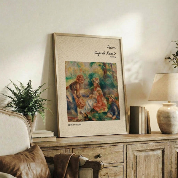 May include: Framed art print of Renoir's impressionist painting showing figures in a pastoral scene with warm earth tones and soft brushstrokes, displayed on rustic wooden sideboard alongside fern plant, ceramic vase, and stacked books in neutral-toned living room setting