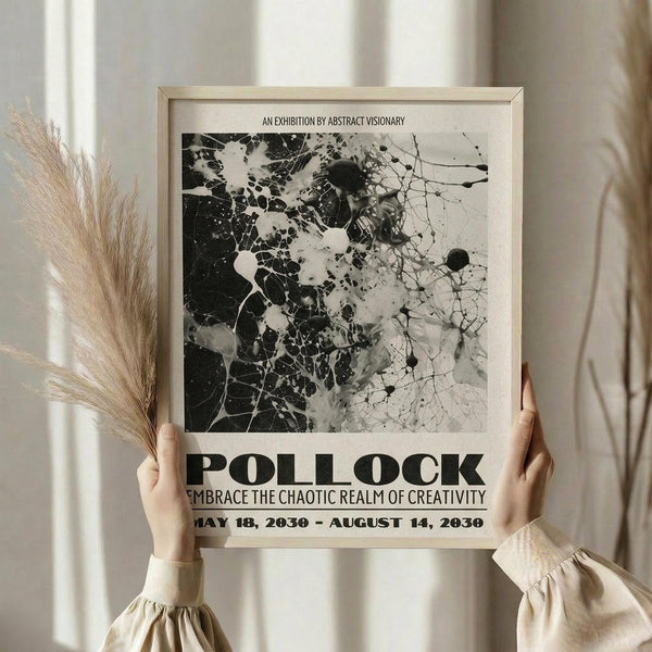 May include: Person in beige clothing holding framed abstract art poster featuring black and white Jackson Pollock-style paint splatters and drips. Poster displays exhibition text including "POLLOCK" and "EMBRACE THE CHAOTIC REALM OF CREATIVITY" with dates. Light wood frame against neutral curtained background with dried pampas grass visible on left side.