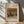 May include: Framed art print featuring Renoir's still life painting of a striped green and yellow melon with peaches on a table, displayed on light wooden floor against white wall with palm leaf shadows cast across the scene.