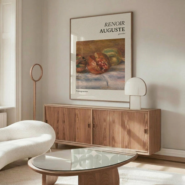 May include: Renoir art poster displaying painted pomegranates in warm reds and greens, framed and hung above a wooden sideboard in a minimalist living room with cream walls, white upholstered chair, glass coffee table, and modern brass floor lamp