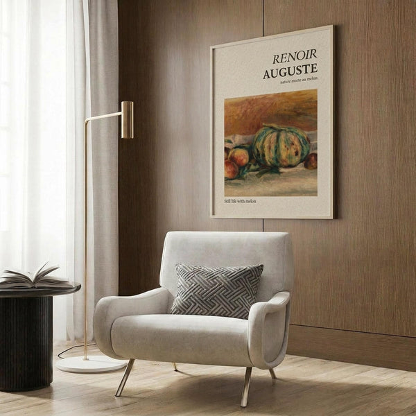 May include: Beige armchair with geometric patterned pillow positioned next to gold floor lamp in modern living room. Framed art poster showing Renoir still life painting with melon and fruits hangs on wood-paneled wall. Natural lighting from window with sheer curtains, dark round side table with open book visible.