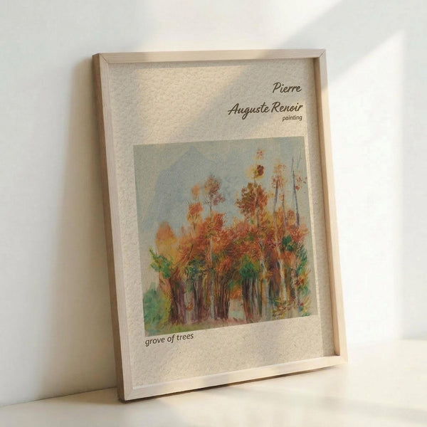May include: Framed art print showing an impressionist painting of autumn trees with orange, red, and green foliage against a pale blue sky. The artwork is displayed in a light wood frame with white matting, featuring text identifying it as a Pierre Auguste Renoir painting titled "grove of trees." The frame leans against a white wall on a light surface.