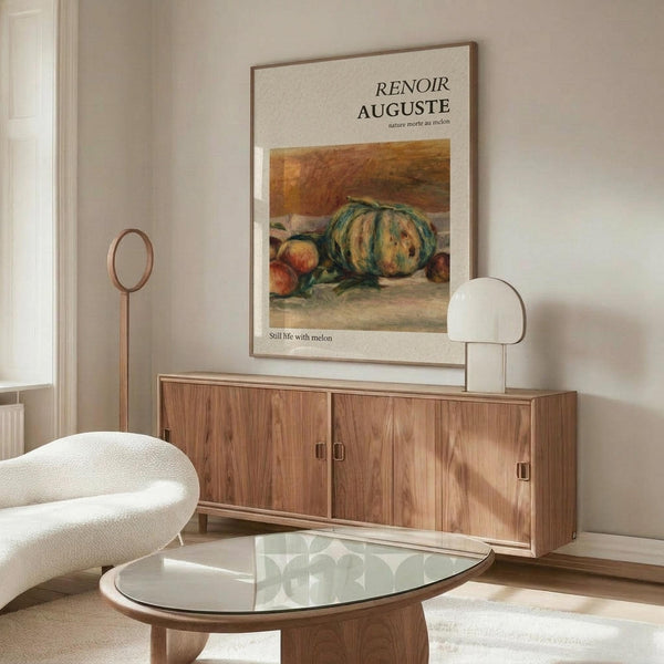 May include: Framed Renoir still life poster featuring green striped melon and fruits in warm earth tones, displayed above walnut sideboard in minimalist living room with cream chair, glass coffee table, and white table lamp. Soft natural lighting creates gentle shadows on pale walls.