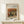 May include: Framed art print featuring Renoir's still life painting of a striped green and yellow melon with peaches on a table, displayed on light wood furniture with a small white wrapped gift beside it. Warm earth tones throughout the classical impressionist artwork in natural wood frame against cream wall.