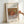 May include: Framed art print featuring Renoir's impressionist painting of split pomegranates with ruby red seeds visible, accompanied by green fruits on draped fabric. The artwork shows warm earth tones and soft brushstrokes typical of the period. Print has white matting with "RENOIR AUGUSTE" and "grenades" text above the image, "Pomegranates" below. Natural wood frame held by hand against white wall, showing realistic room display mockup.