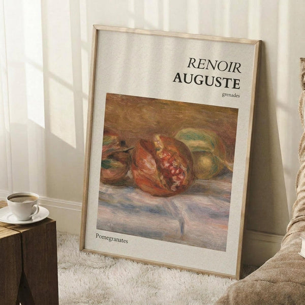 May include: Framed art print featuring Renoir's impressionist painting of ripe pomegranates in warm red and orange tones against a muted brown background. The poster has cream matting with "RENOIR AUGUSTE" and "grenades" text above the artwork and "Pomegranates" below. Light wood frame leans against white paneled wall on textured cream rug, with wooden block holding white coffee cup nearby and beige fabric visible.