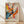 May include: Framed abstract art print in wooden frame leaning against white wall on light wood floor. Artwork features energetic paint splatters, drips and brushstrokes in vibrant orange, blue, yellow, pink and black against cream background. Text below reads "POLLOCK Expressive Expressionist Movement" in bold letters. Natural lighting creates soft shadows on textured white wall.
