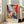 May include: Vibrant abstract art poster in light wooden frame leaning against white wall next to beige upholstered sofa. Artwork features explosive swirls of orange, blue, pink, yellow and white paint in dynamic flowing patterns. Text below reads "POLLOCK Expressive Expressionist Movement" on cream background. Bright natural light streams through tall windows creating soft shadows on hardwood floor.