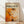 May include: Framed abstract art poster with orange and white paint splatters in Jackson Pollock's drip painting style, displayed against white wall on light wooden floor. Text reads "Chaos and Creativity 1912-1956 Pollock" above energetic brushstrokes and paint drips in warm autumn tones with black accents.
