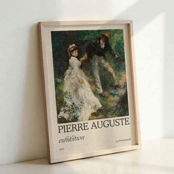 May include: A framed exhibition poster featuring Renoir's "La Promenade" from 1870, showing a woman in a flowing white dress and a man in dark clothing walking through a lush green landscape. The poster has white text reading "PIERRE AUGUSTE exhibition" below the impressionist painting. The light wood frame leans against a white wall, casting soft shadows in natural lighting.