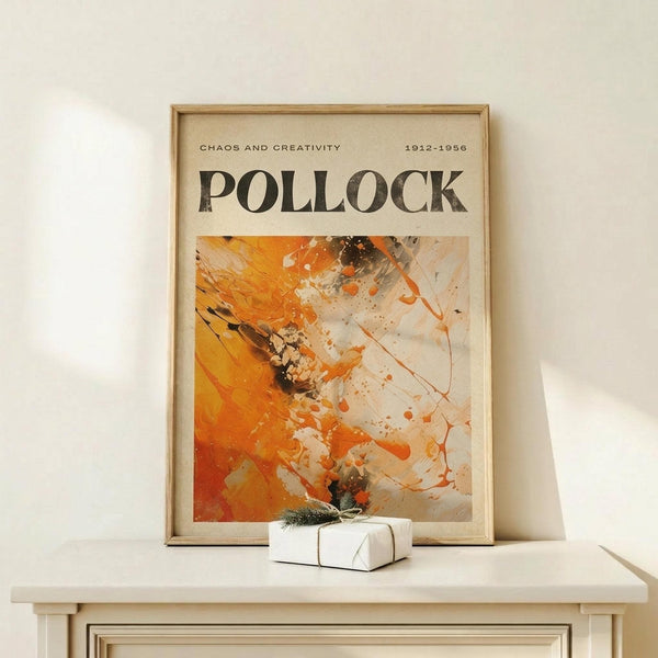 May include: Framed abstract art poster featuring bold orange and white paint splatters with black accents in Jackson Pollock's signature drip style, displayed on light wood console table next to small wrapped gift with evergreen sprig against cream wall