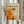 May include: Person in cream blouse holding framed abstract art poster featuring orange, white, and black paint splatters in Jackson Pollock's drip painting style. Poster displays "CHAOS AND CREATIVITY" and "1912-1956" text above "POLLOCK" in bold letters. Light wood frame against white curtained background with dried pampas grass visible on left side.
