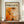 May include: Framed abstract art print in warm orange, white, and dark tones with paint splatters and dynamic brushstrokes, displayed on wooden sideboard next to white ceramic vase and stacked books. The poster features "POLLOCK" in bold black letters above the artwork with "CHAOS AND CREATIVITY 1912-1956" header text. Modern interior setting with white paneled walls and neutral decor.