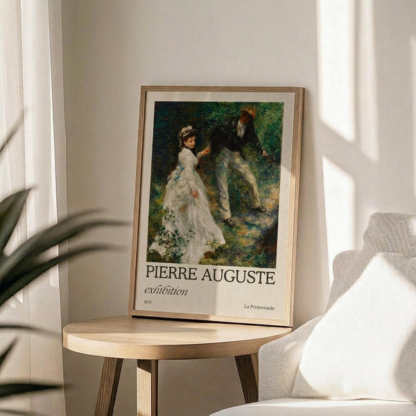 May include: Framed exhibition poster featuring Pierre-Auguste Renoir's "La Promenade" from 1870, showing a woman in a flowing white dress and man in dark clothing walking through dappled green forest sunlight. The poster sits on a light wood round side table next to a cream upholstered chair, with soft natural lighting and plant shadows creating an elegant, minimalist interior setting.