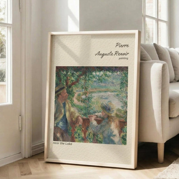 May include: Framed poster print leaning against white wall next to beige armchair in bright living room. Print shows Impressionist-style painting of figures by lakeside with lush green foliage, rendered in soft blues, greens, and earth tones. Light wood frame with cream matting. Natural sunlight streams through windows onto hardwood floors.
