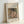 May include: Framed art print displayed on white surface against white wall. Light wood frame contains reproduction of impressionist painting showing woman in pink dress and dark feathered hat, resting chin on hand while holding delicate teacup. Soft, muted colors in classical French painting style. Text above reads "Pierre Auguste Renoir painting" and below "cup of chocolate" on cream textured background.