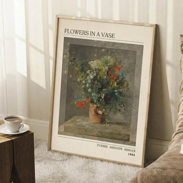May include: Framed art print leaning against white wall corner showing floral still life painting with wildflowers in earthenware vase. Print has cream matting with black text identifying artist and date. Scene includes wooden side table with white coffee cup, beige throw blanket, and white textured rug. Natural lighting creates soft shadows on wall.