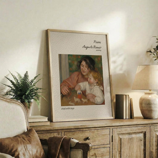 May include: Framed reproduction of Renoir's "Child with Toys" showing a woman in coral dress holding a blonde child with small toy figures, displayed on rustic wooden sideboard alongside fern plant, ceramic vase, and books in warm neutral living room setting.