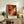 May include: Abstract expressionist art print with vibrant orange, red, black and white paint swirls in light wood frame, displayed on rustic wooden sideboard alongside fern plant, books, ceramic vase and lamp in cozy living room setting with beige armchair